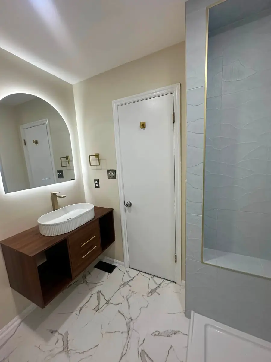 Finished bathroom with floating wood vanity, round mirror and marble-look tile